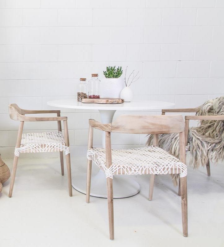 White round dining table with natural timber chairs featuring white woven seats, creating a contemporary and relaxed dining setting.