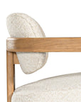 Stylish wooden occasional chair with boucle upholstery, set in a minimalist dining space with a sculptural stone table and an olive tree in a textured planter