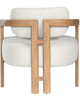 Stylish wooden occasional chair with boucle upholstery, set in a minimalist dining space with a sculptural stone table and an olive tree in a textured planter