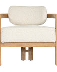 Stylish wooden occasional chair with boucle upholstery, set in a minimalist dining space with a sculptural stone table and an olive tree in a textured planter