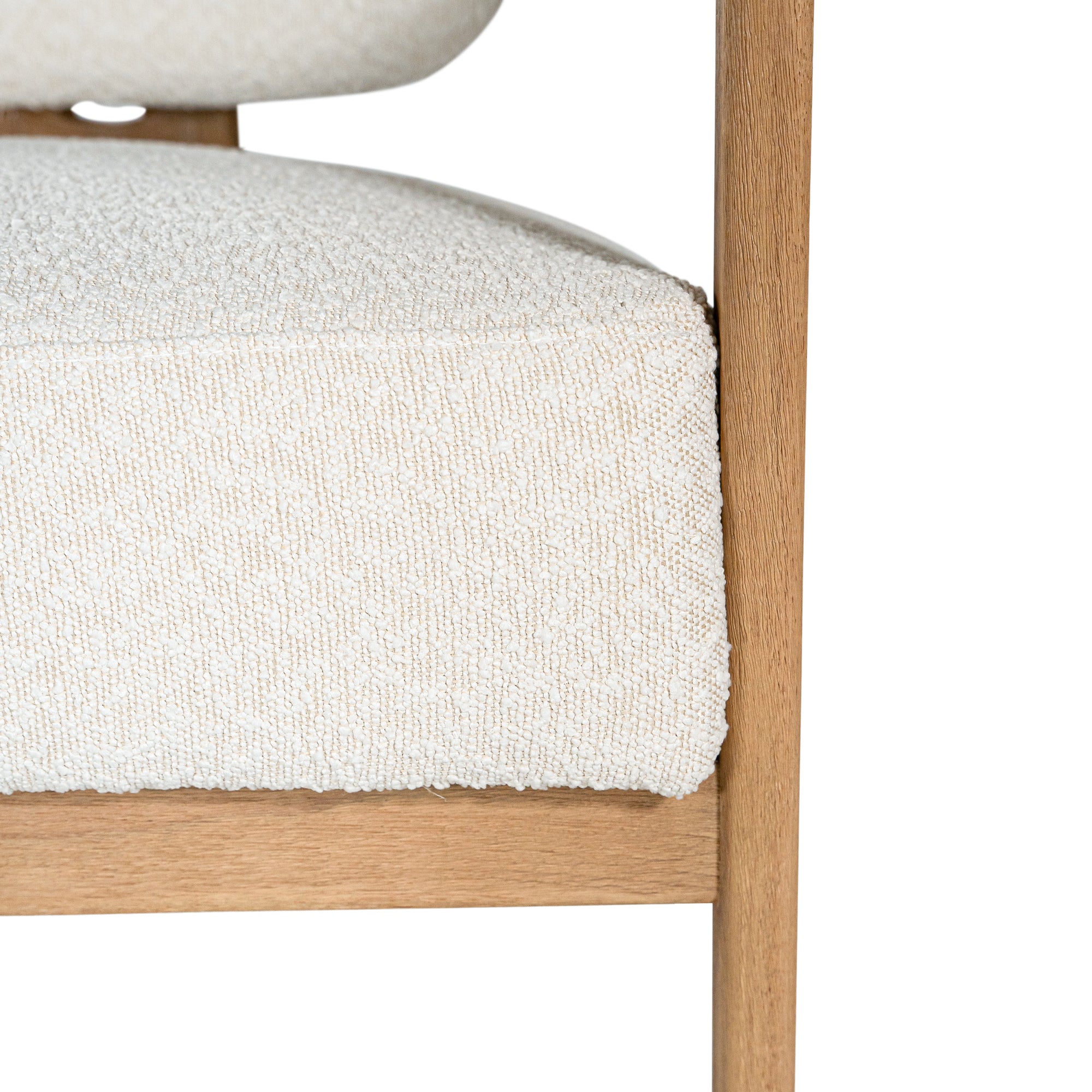 Stylish wooden occasional chair with boucle upholstery, set in a minimalist dining space with a sculptural stone table and an olive tree in a textured planter