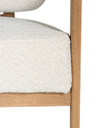 Stylish wooden occasional chair with boucle upholstery, set in a minimalist dining space with a sculptural stone table and an olive tree in a textured planter