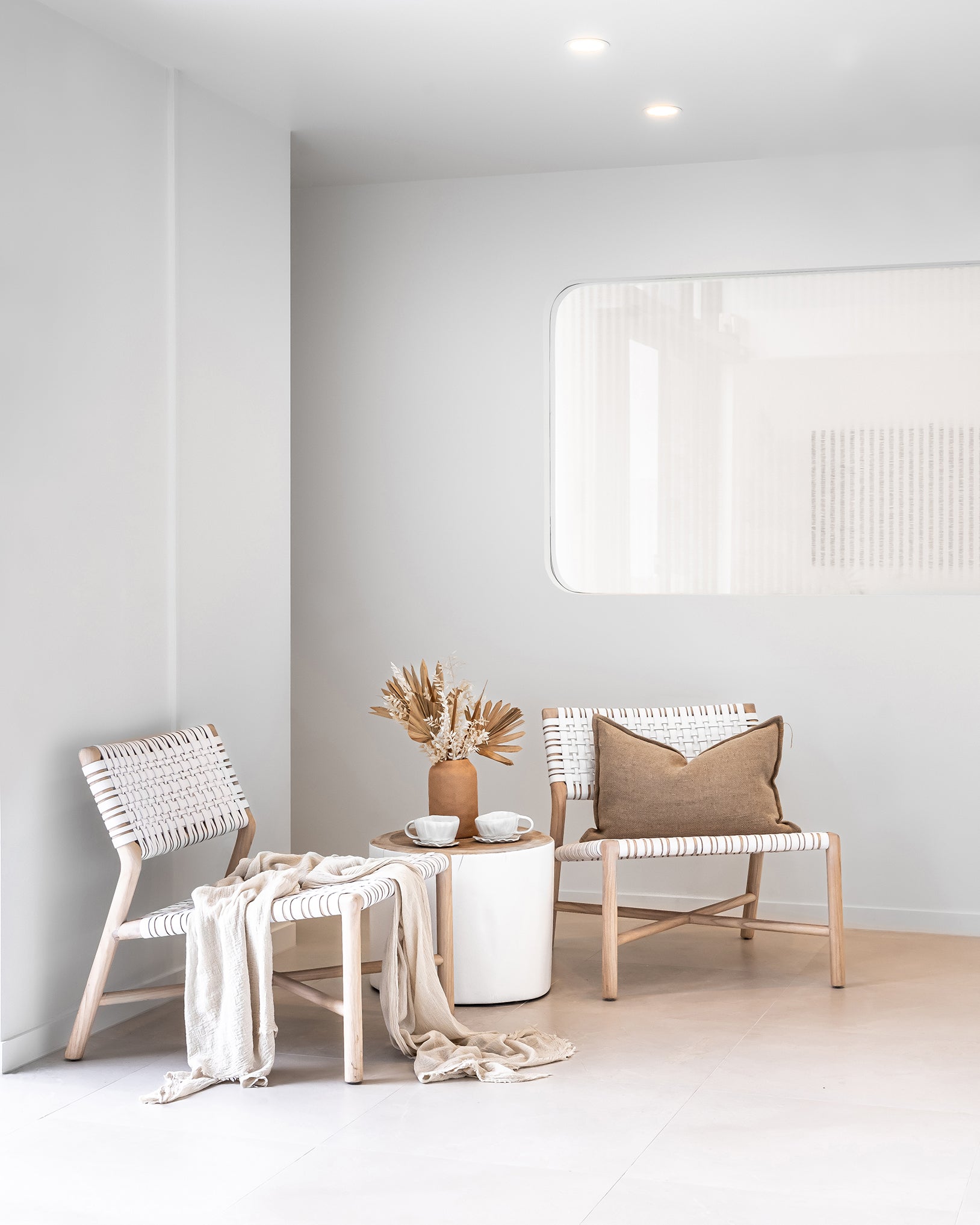 A serene lounge setting featuring natural wood lounge chairs with woven white leather seats and backrests, styled with neutral textiles and earthy décor
