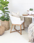 KULALA Living handwoven rattan dining chair with a curved backrest, natural wood legs, and a white seat cushion, blending coastal and contemporary design