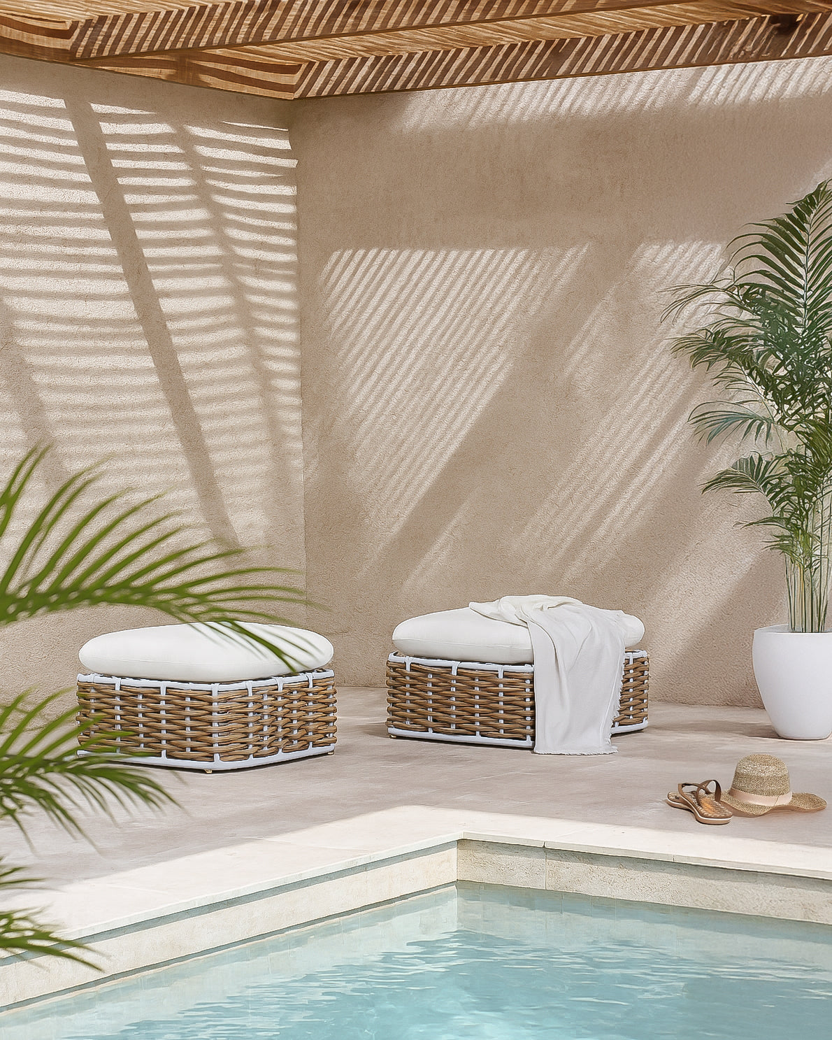 Zahara Ottoman featuring handwoven rattan weave with white cushion, styled poolside under slatted timber shade with palm plants and soft natural light