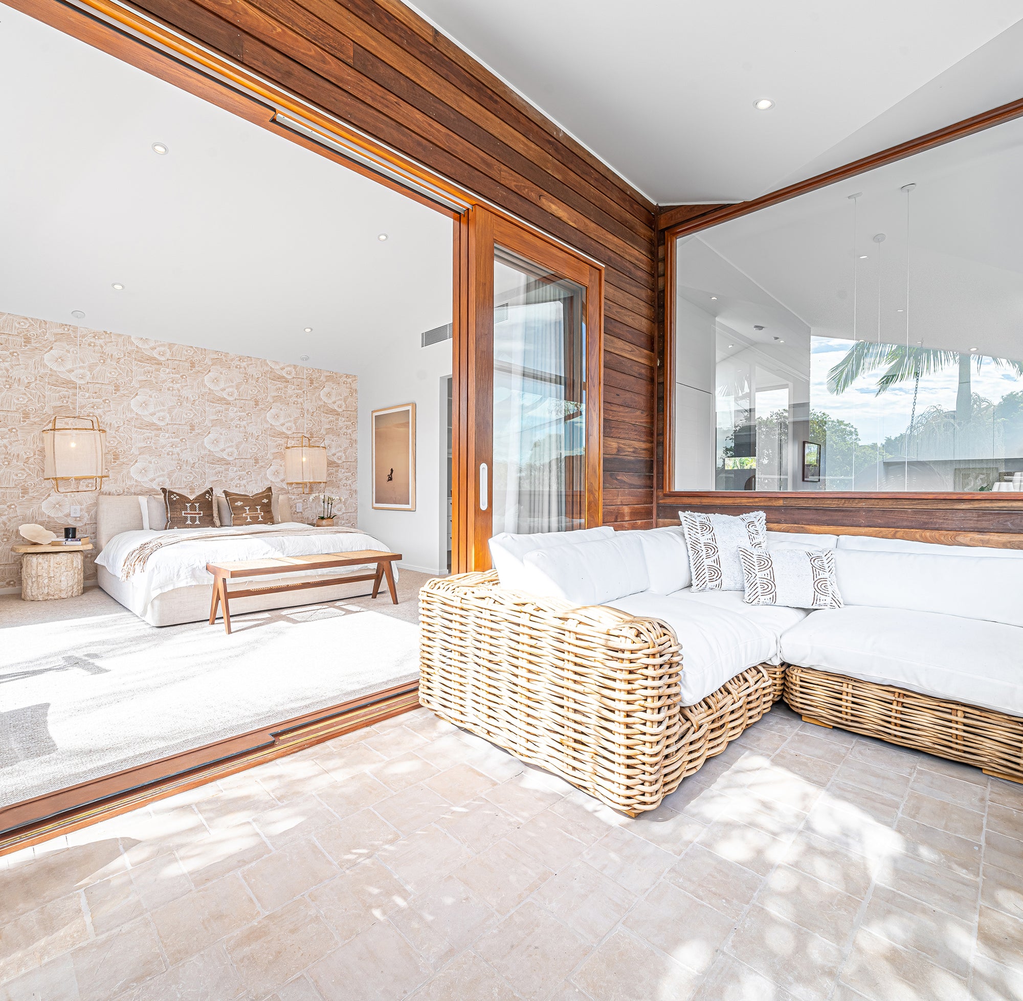 Coastal-inspired bedroom with natural wicker corner sofa featuring white cushions, complemented by a wooden bench and pendant lighting