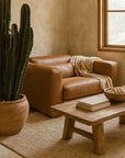 Leather Armchair in tan leather styled with a throw in a modern living room featuring a timber coffee table, cactus planter, and neutral textured rug