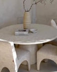 Dining room with a sculptural travertine table, textured upholstered chairs, and a handcrafted paper mâché vase, creating a serene and elegant space