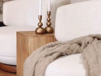 A beautifully styled living space featuring KULALA Living’s brass candlestick holders on a sculptural wooden side table. The warm, neutral tones of the boucle swivel chair, soft throw, and textured rug create an inviting and sophisticated setting with organic elegance