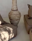 Earthy lounge setting featuring a rustic clay vase with branch arrangement, complemented by natural-toned low-profile lounge seating and a relaxed, minimalist aesthetic.