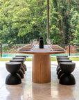Elegant outdoor dining scene featuring a handcrafted teak table paired with black hourglass stools, overlooking lush greenery and a serene pool.