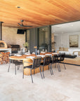 Outdoor entertaining area featuring sculptural black stools, woodfire pizza oven, and oak island bench styled for dining.
