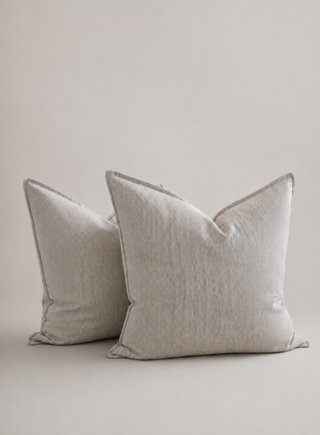 Two square throw pillows in a light beige linen-like fabric, arranged against a plain beige background.