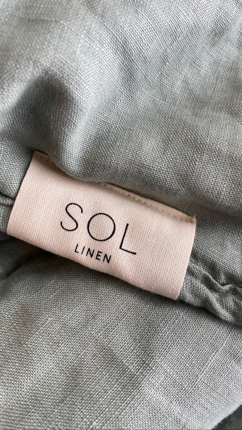SOL Linen Sea Mist quilted coverlet in soft linen fabric, shown draped on a bed with a textured, cozy look.