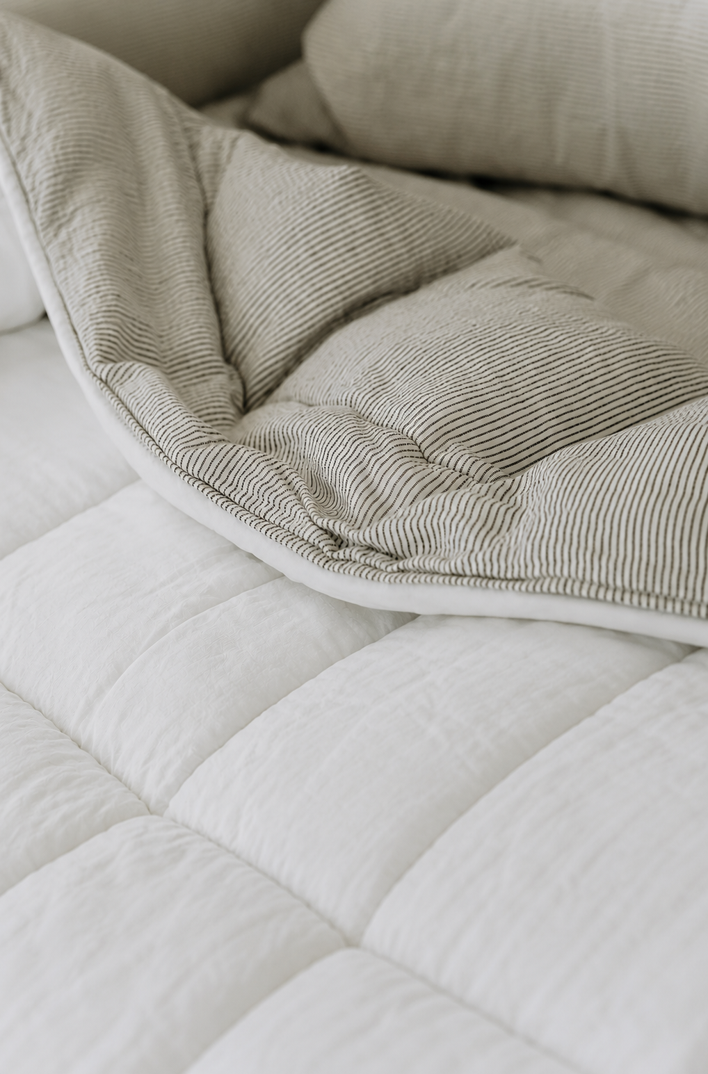 SOL Linen white and ink pinstripe linen quilted coverlet on a bed, showcasing its elegant bedding design and textured fabric.