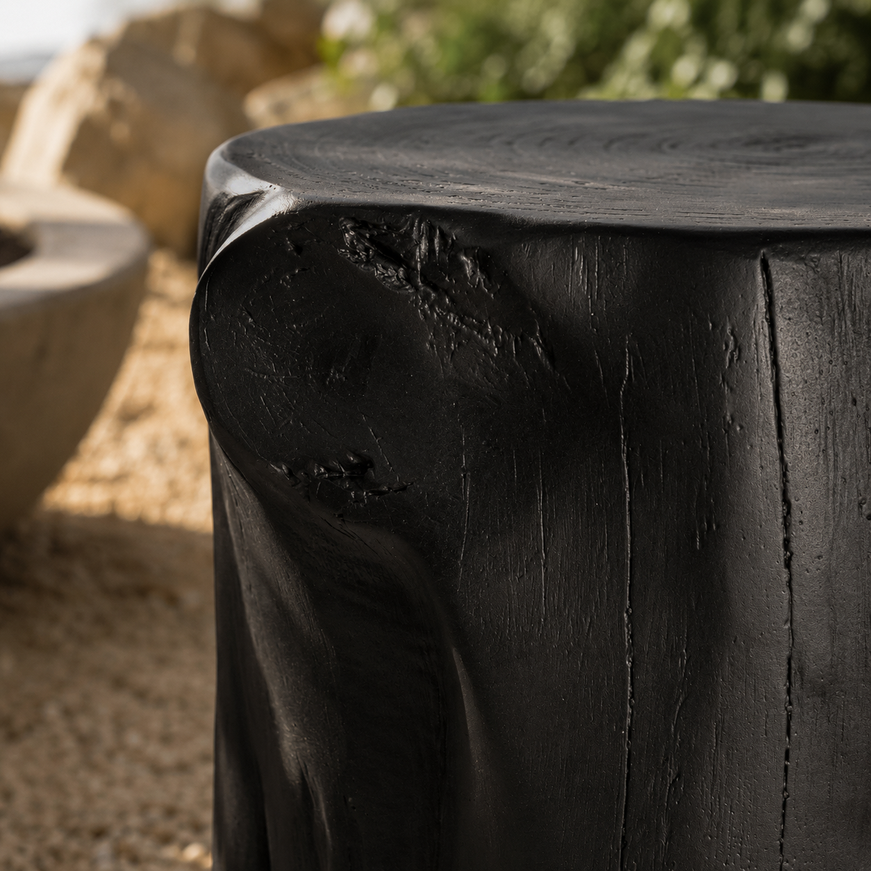 Black magnesium oxide stools arranged around an outdoor fire pit in a coastal garden retreat, creating a relaxed gathering space framed by native greenery and ocean views.