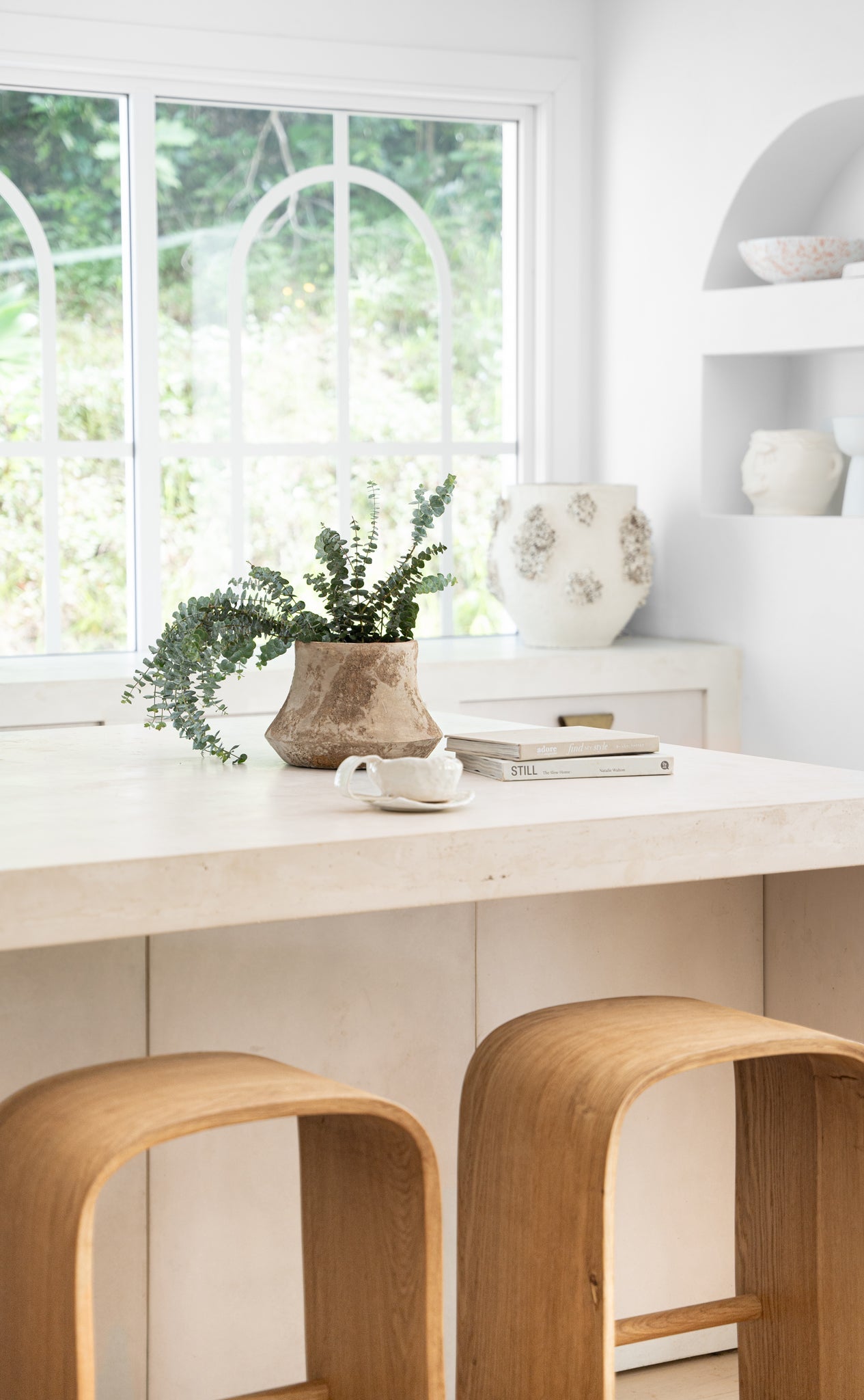 KULALA Living Elula Counter Stools in natural oak featured in a contemporary white kitchen with curved travertine benchtop and rustic accents