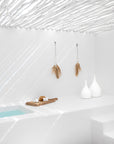 Serene outdoor day spa featuring a white rendered bath, natural timber bath tray, decorative white vases, and pampas grass wall hangings beneath sculptural white ceiling rafters.
