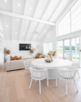 Bright white living space featuring a round dining table surrounded by white rattan chairs, styled with neutral de